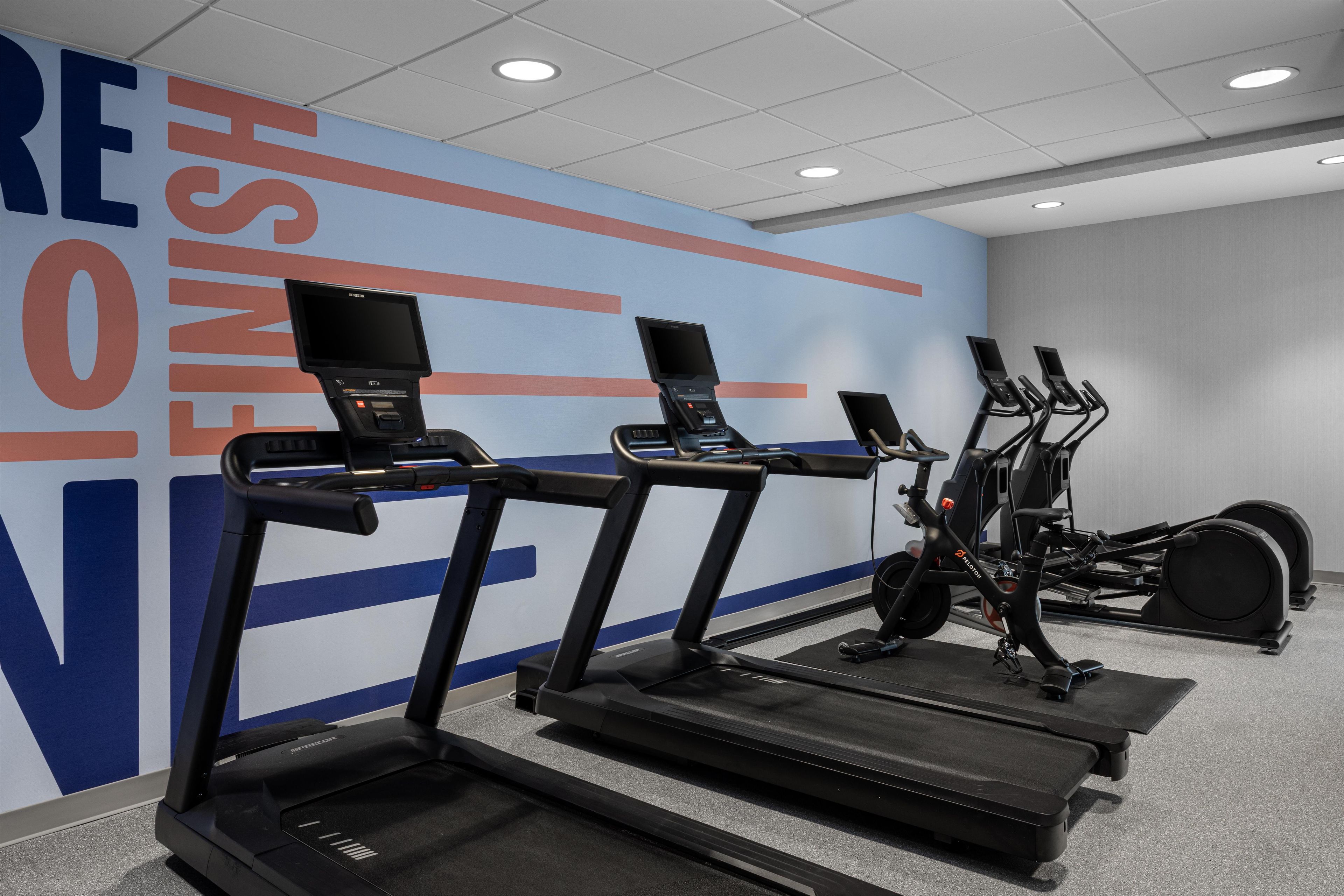 Un espacio de fitness con cintas de correr, bicicletas estáticas y una pared con mensajes motivacionales.