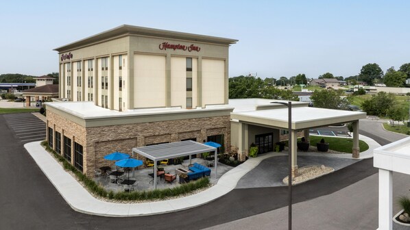 A Hampton Inn hotel with a modern facade, outdoor seating area, and a parking lot.