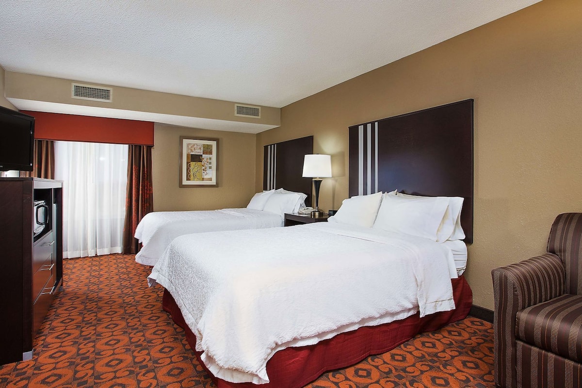 A hotel room with two beds, a desk, a chair, a television, and a patterned carpet.