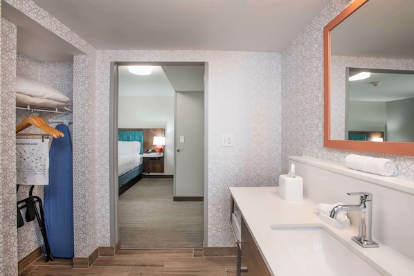 A hotel room with a walk-in closet, a bathroom with a sink and mirror, and a bed with a nightstand.