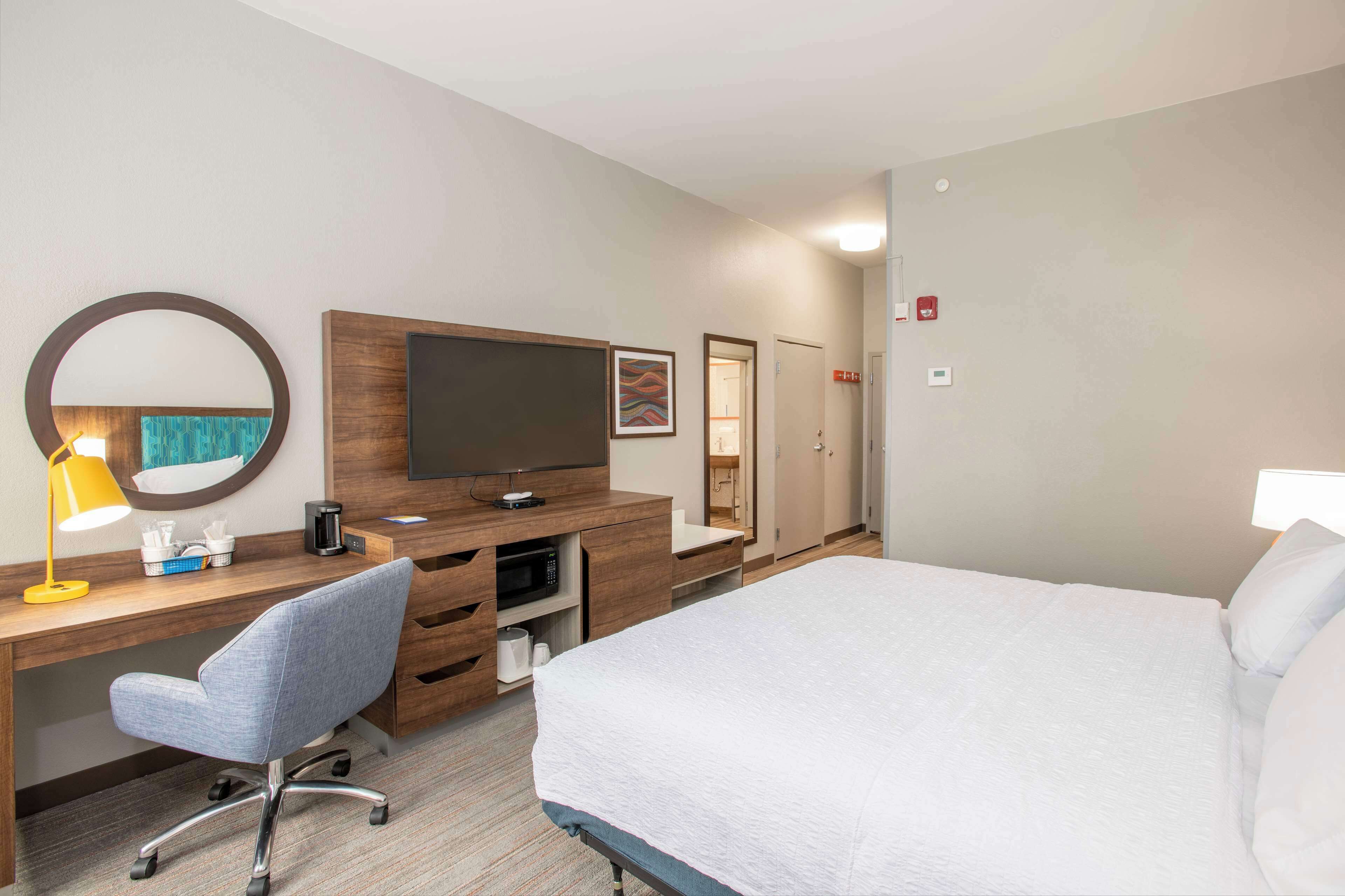 A hotel room with a bed, a desk with a chair, a television, a microwave, and a mirror.