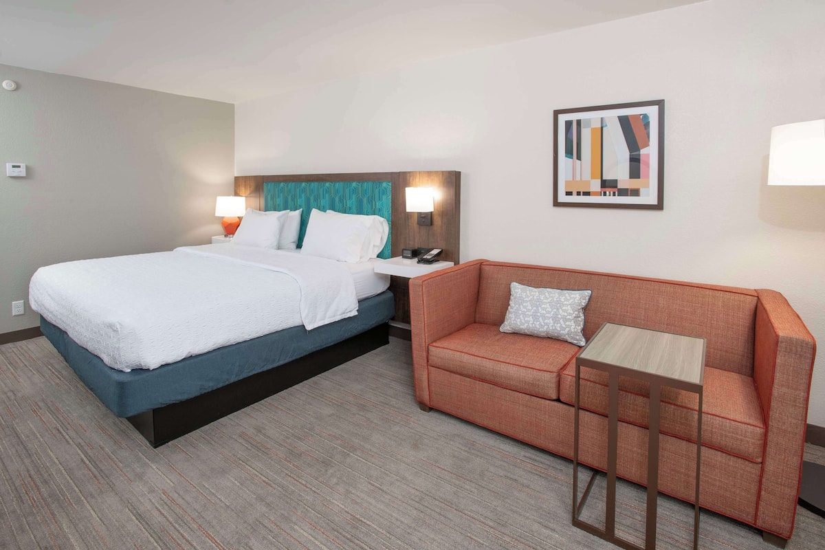 A hotel room with a bed, a sofa, a small table, and a wall-mounted lamp.