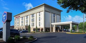 A Hampton Inn hotel with a modern facade, a covered entrance, and a parking lot with several cars.