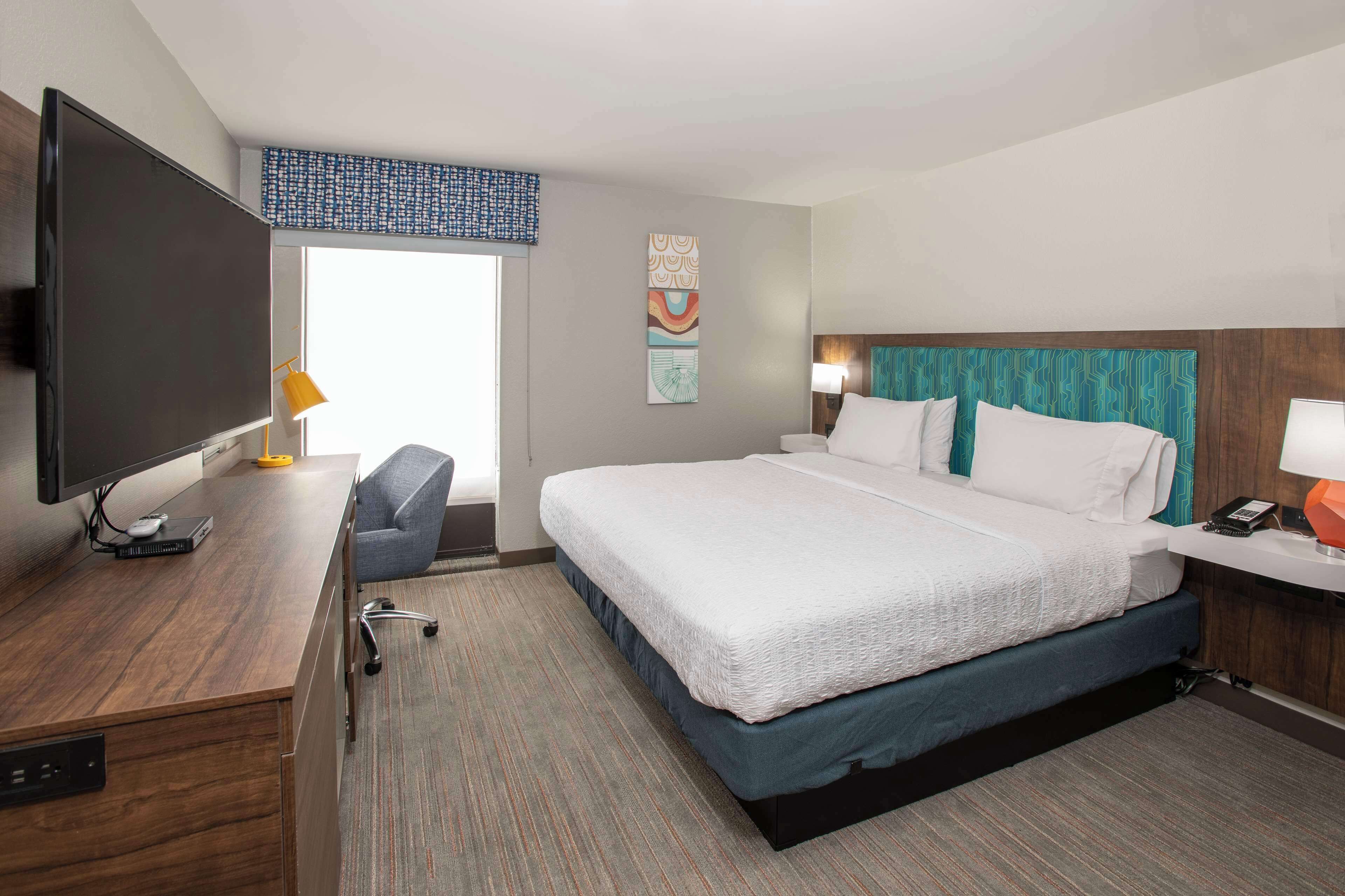 A hotel room with a large bed, a desk with a computer, a TV, and a chair.