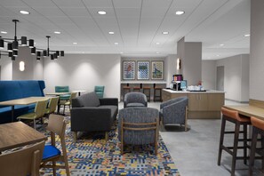 A modern hotel lobby with a seating area, a bar, and a coffee station.
