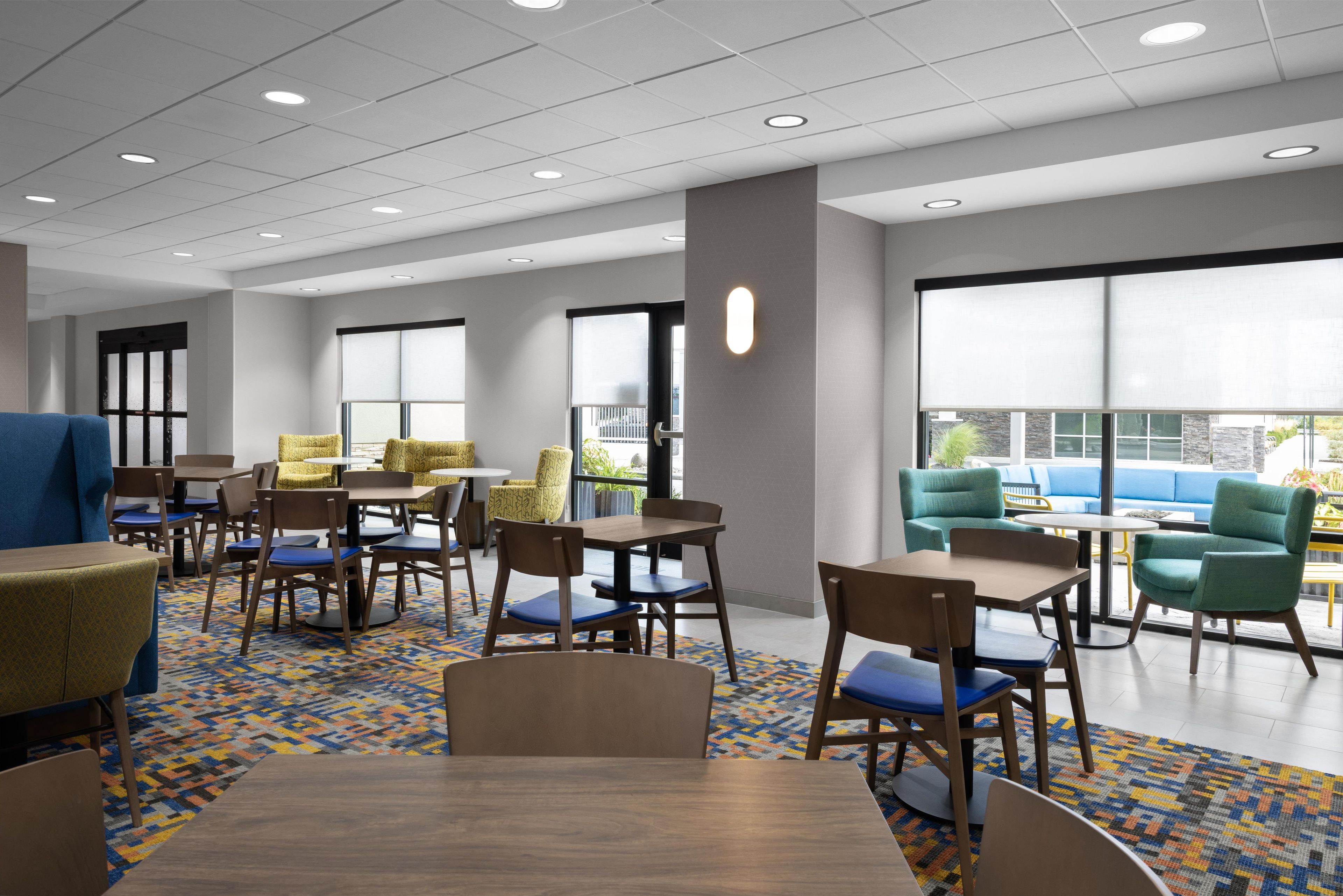 A modern dining area with multiple tables and chairs, large windows, and a view of the outdoors.