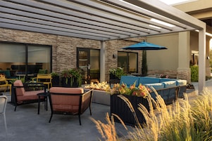 Un patio al aire libre con mobiliario, una chimenea y una zona cubierta con un pérgola.