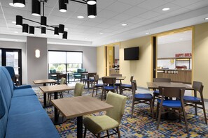 A modern dining area with multiple tables and chairs, a large window, and a breakfast bar.