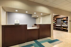 A hotel reception area with a counter, a sign for Hilton Honors, and a snack bar in the background. - Hampton Inn Denville/Rockaway/Parsippany (Denville)