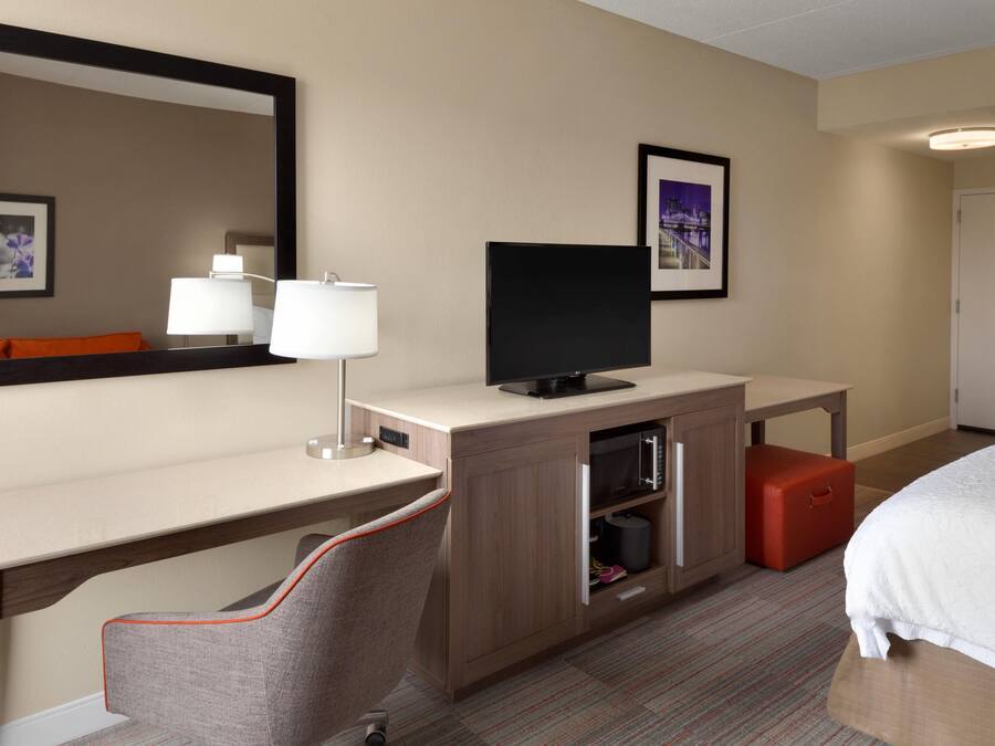 Une chambre d’hôtel avec un lit, un bureau avec une télévision, une chaise, un miroir et une porte.