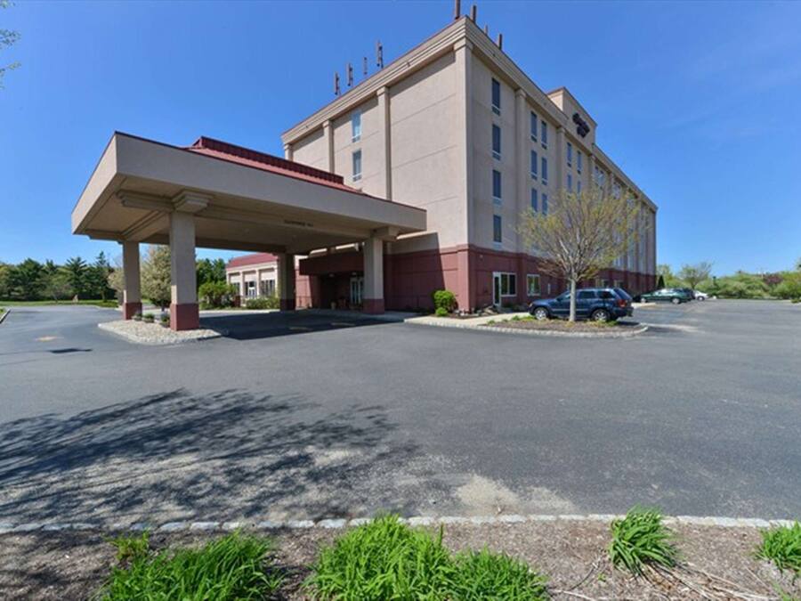 A hotel with a covered parking area, a main building with multiple floors, and a clear sky.