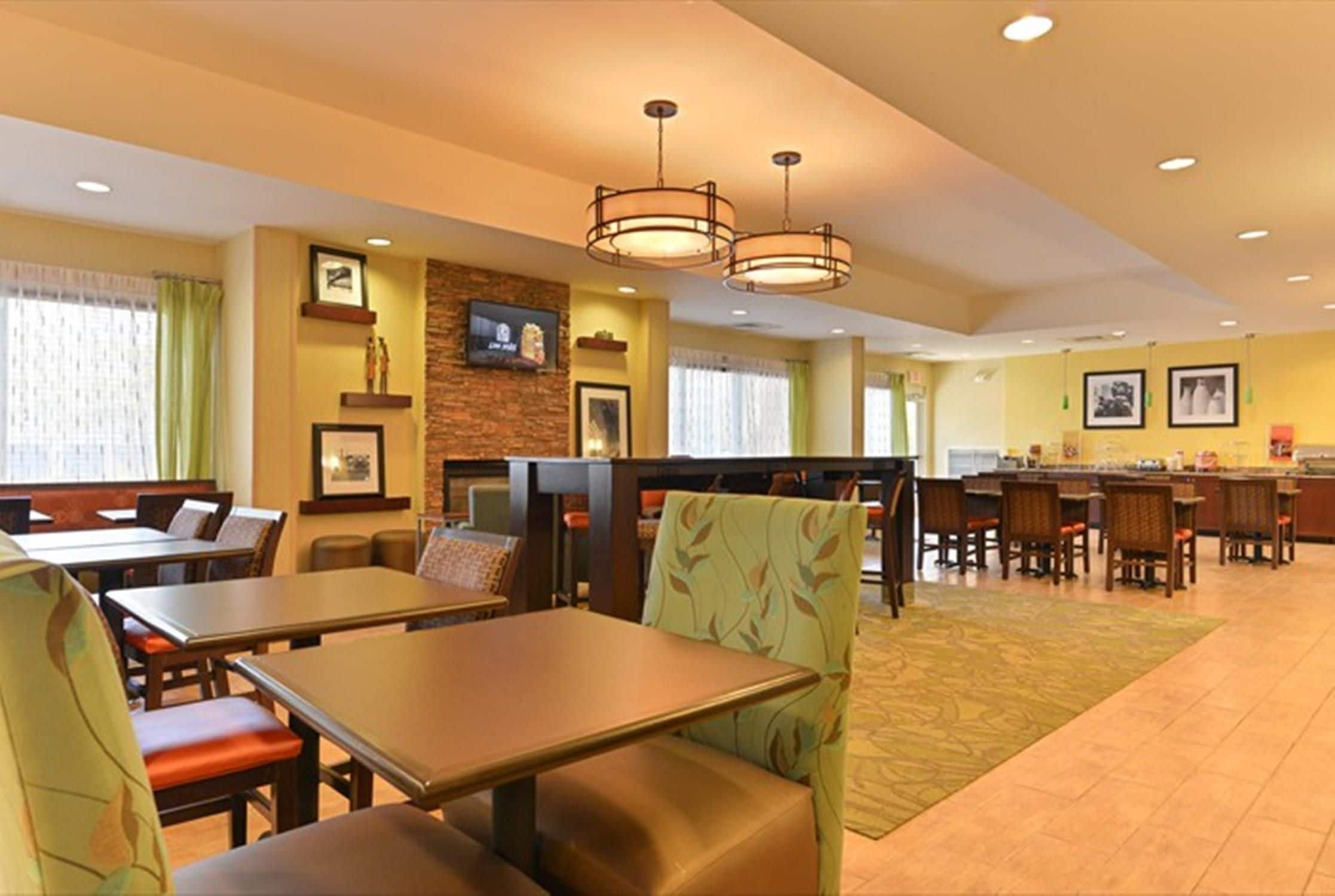 A hotel dining area with tables and chairs, a bar, and a television screen.