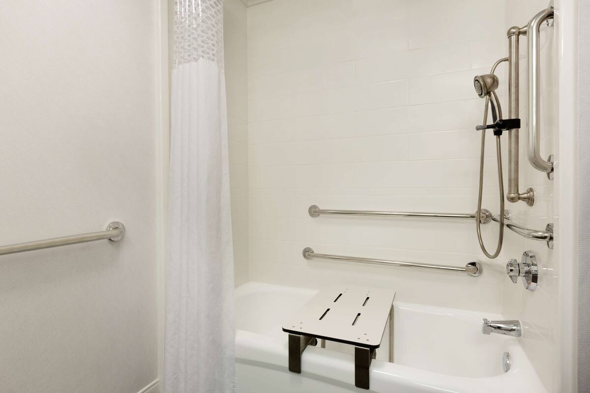A modern bathroom with a bathtub, grab bars, and a shower head.