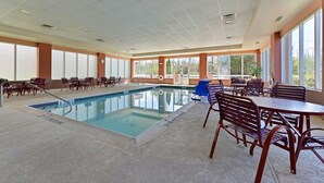 A pool area with a rectangular pool, surrounded by lounge chairs and tables, and large windows providing natural light. - Hampton Inn Denville/Rockaway/Parsippany (Denville)