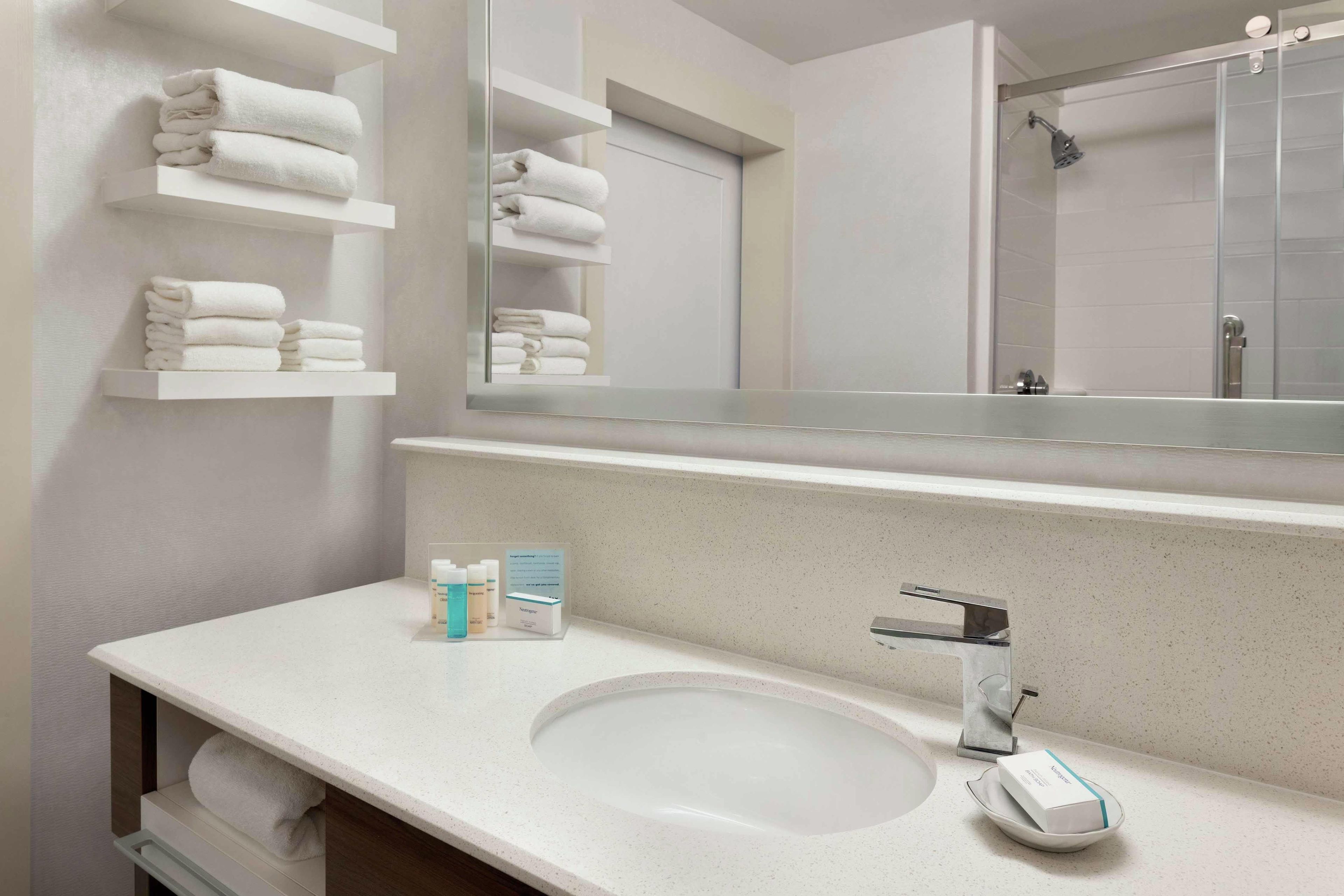 A modern bathroom with a large mirror, white sink, and towel racks.