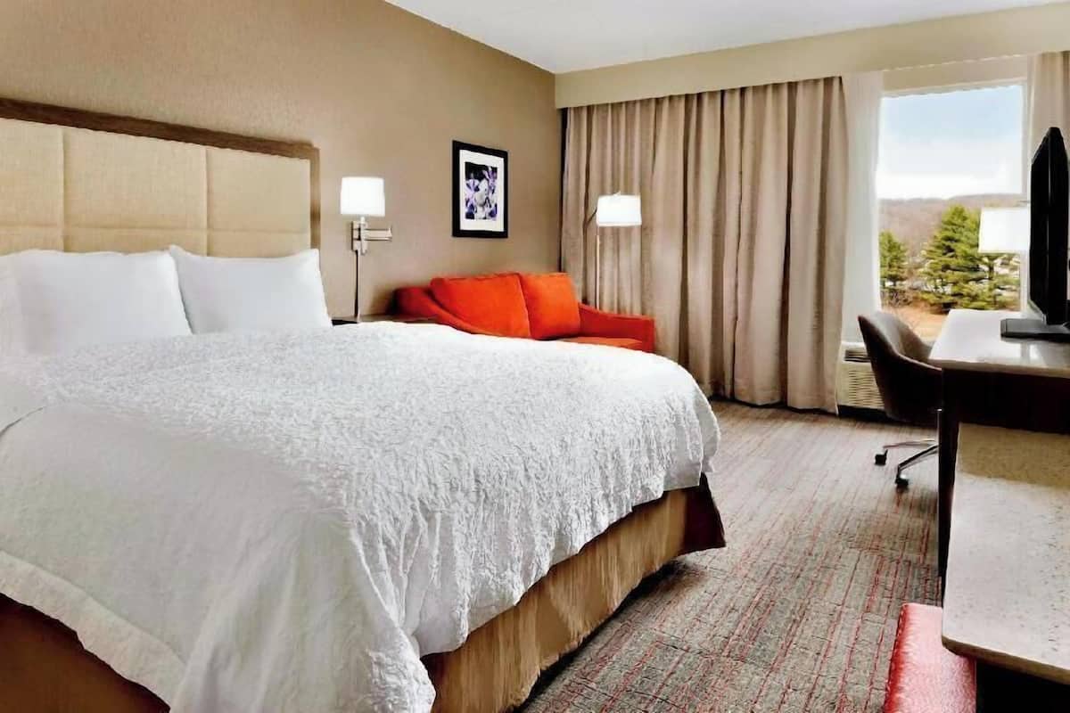 A hotel room with a large bed, a desk, a chair, and a window with curtains.