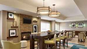 A spacious dining area with a long table, multiple chairs, a fireplace, and a television mounted on the wall. - Hampton Inn Denville/Rockaway/Parsippany (Denville)
