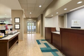 A hotel reception area with a counter, framed artwork, and a view of the entrance. - Hampton Inn Denville/Rockaway/Parsippany (Denville)