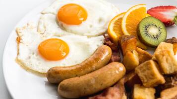 A plate with two sunny-side-up eggs, sausages, bacon, and fresh fruit including kiwi and orange slices.