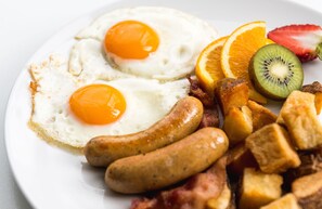 A plate with two sunny-side-up eggs, sausages, bacon, and fresh fruit including kiwi and orange slices. - Hampton Inn Denville/Rockaway/Parsippany (Denville)