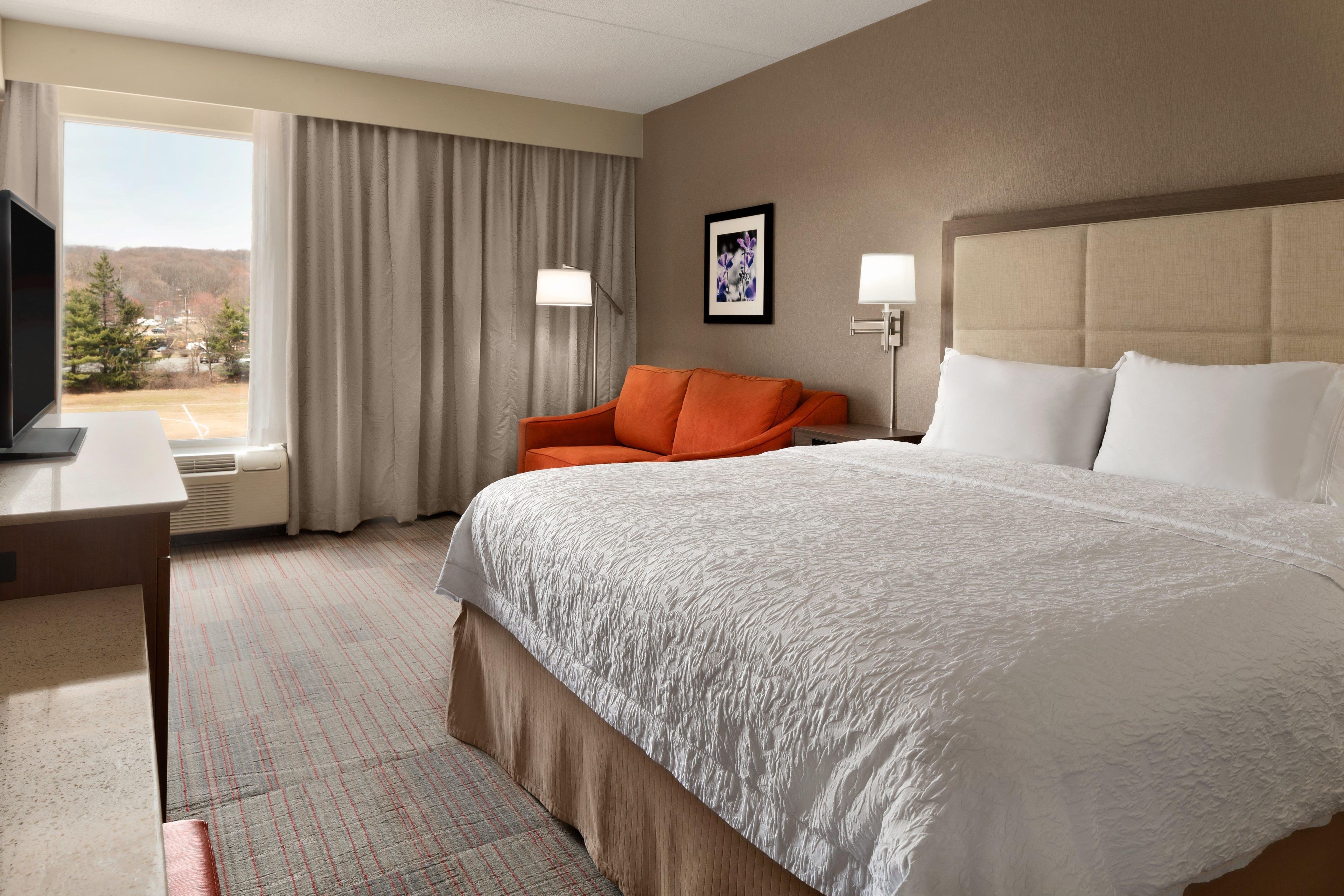 A hotel room with a large bed, a desk, a chair, a television, and a window with curtains.