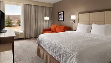 A hotel room with a large bed, a desk, a chair, a television, and a window with curtains.