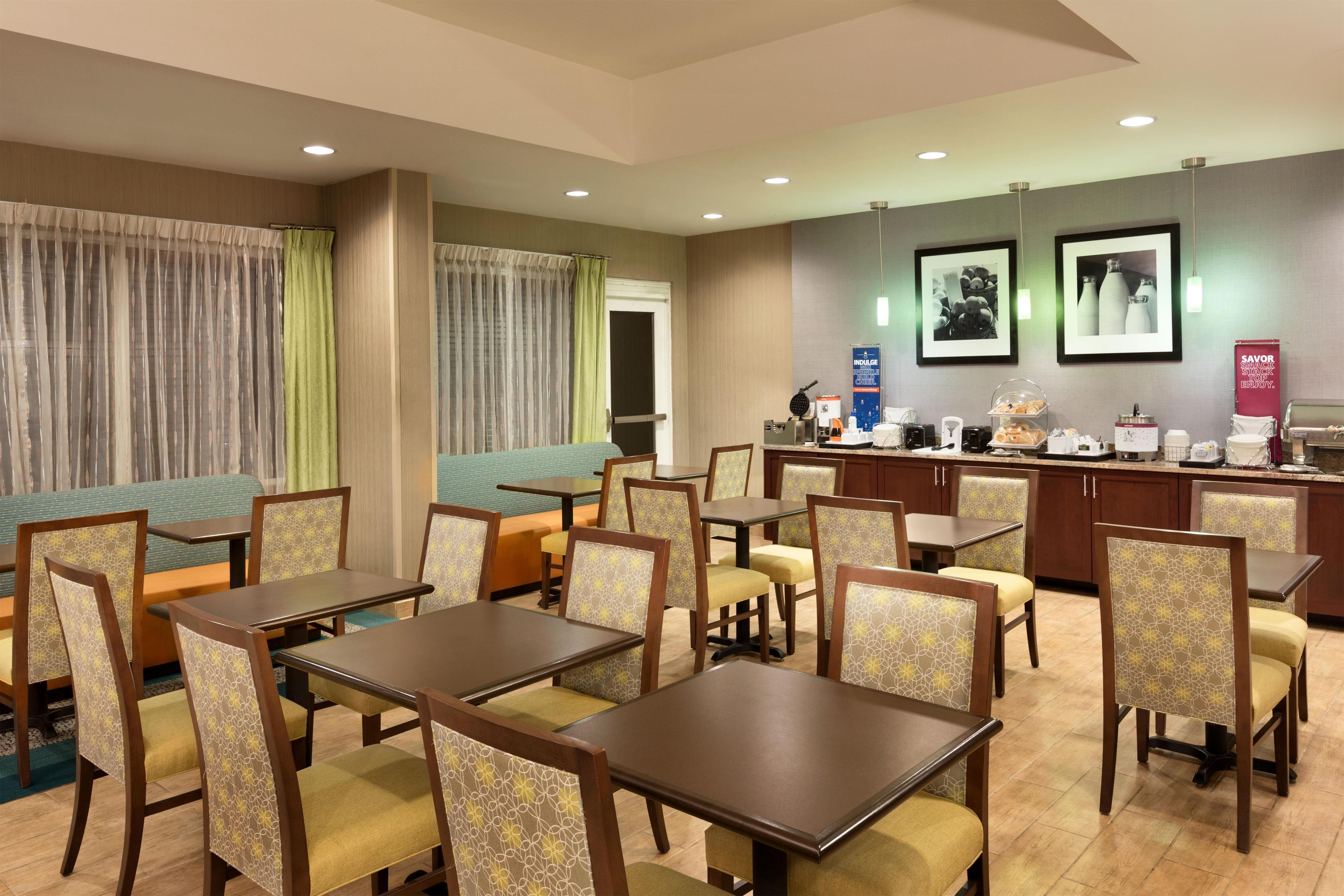 A hotel dining area with tables and chairs, a counter with food items, and a wall with framed pictures.