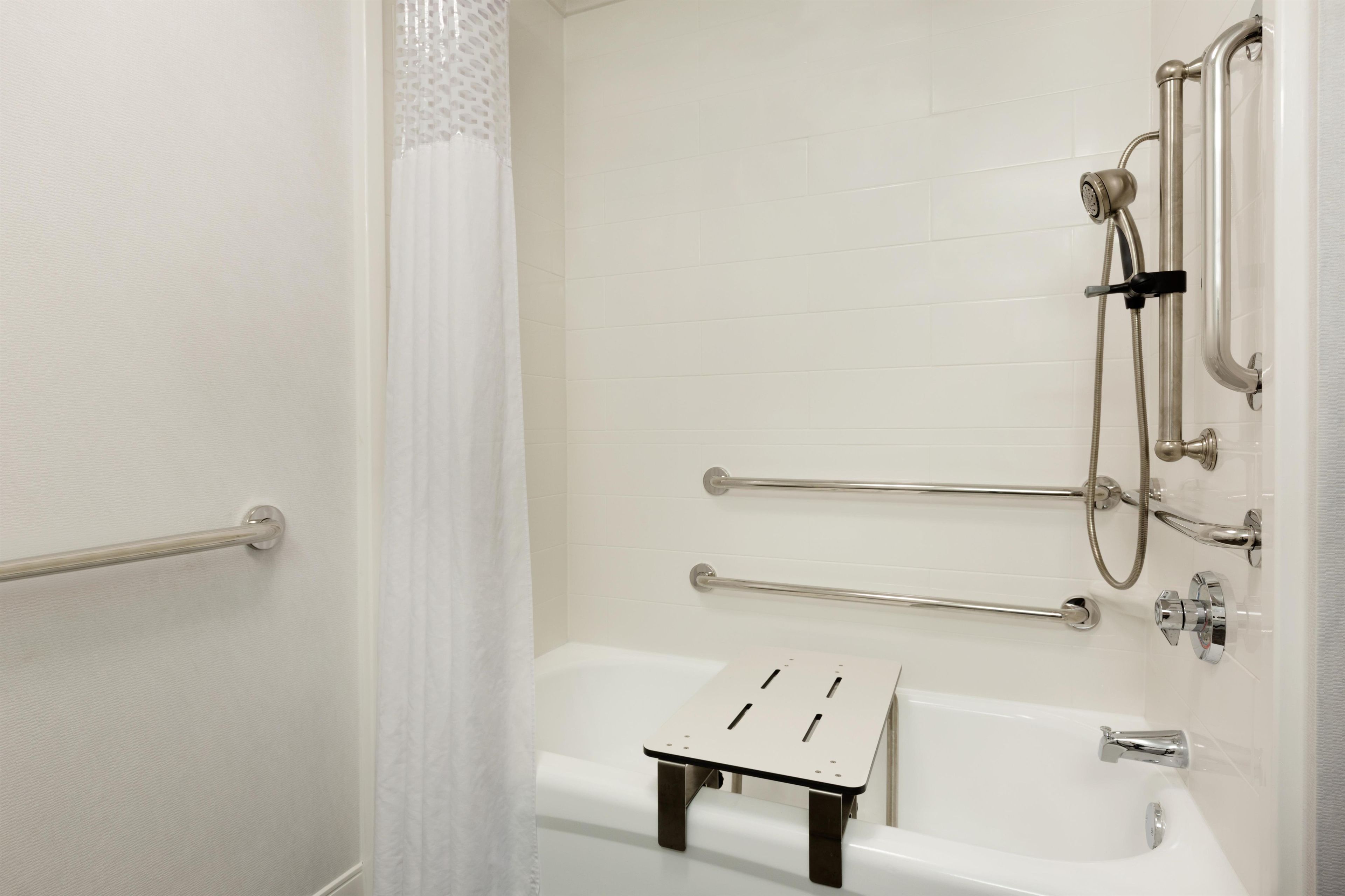 A bathroom with a bathtub, a shower, and a handrail.