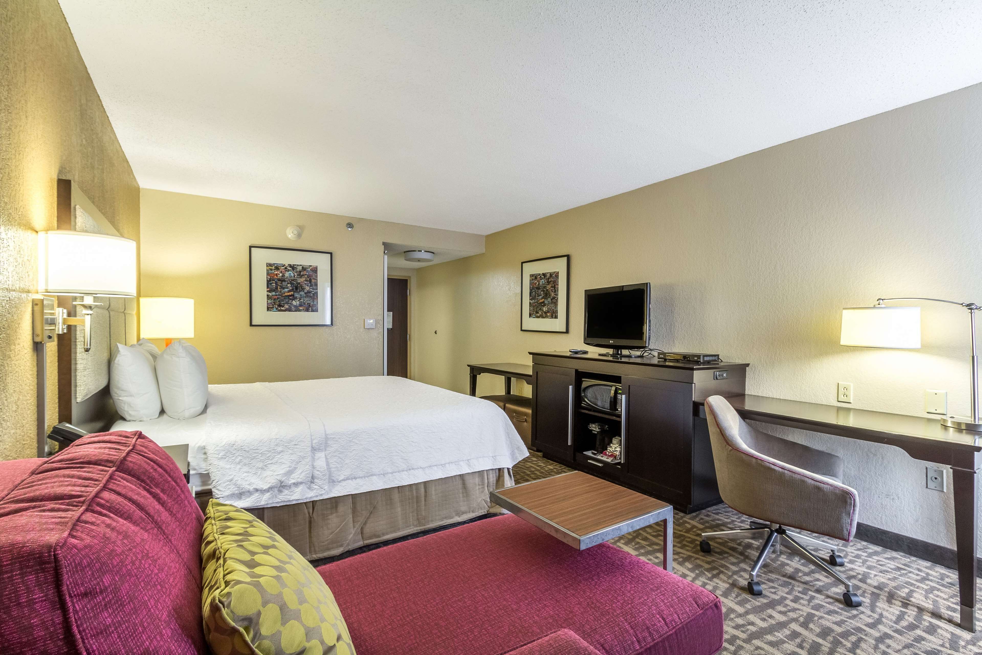 A hotel room with a bed, a desk, a chair, a television, and a lamp.