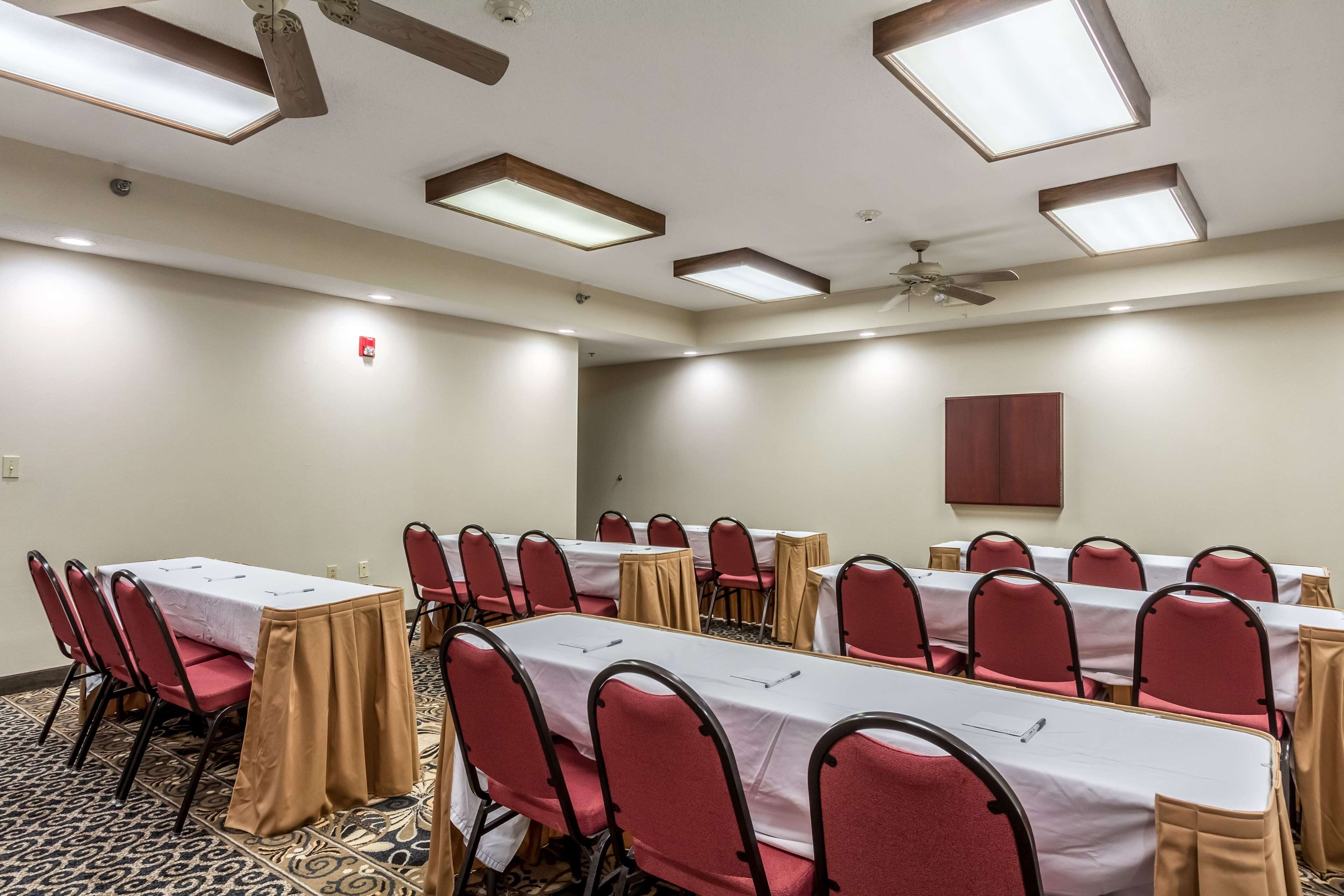A conference room with multiple tables and chairs, equipped with ceiling lights and a ceiling fan.
