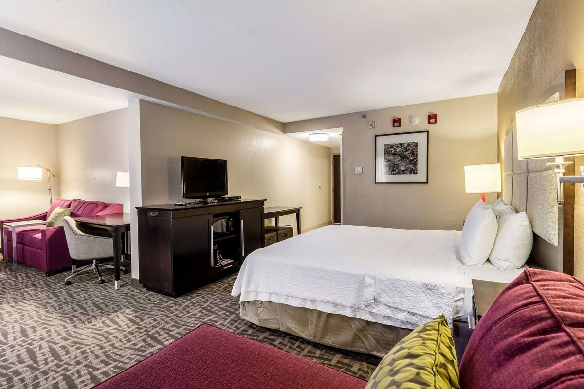 A hotel room with a bed, a desk, a chair, a television, and a lamp.