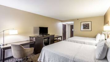A hotel room with a desk, chair, television, two beds, and a framed picture on the wall.