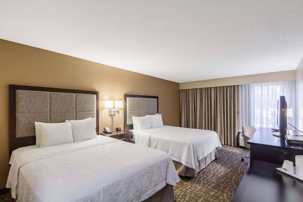 A hotel room with two beds, a desk, a computer, and a telephone.