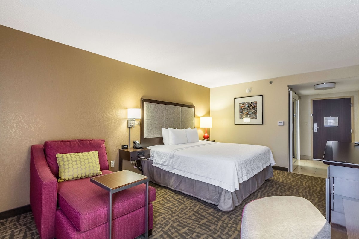 A hotel room with a bed, a desk, a chair, a nightstand, and a lamp.