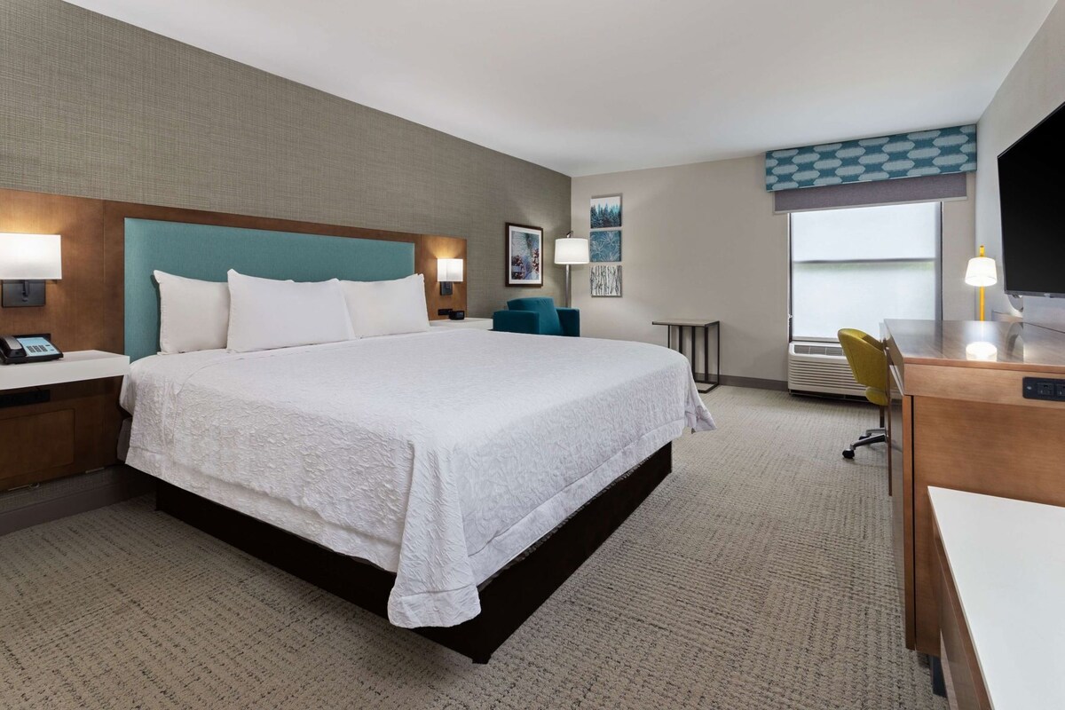 A hotel room with a large bed, bedside tables, a desk, and a TV.