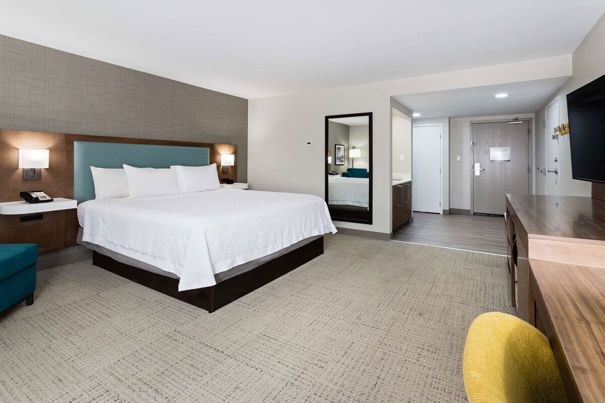 A hotel room with a bed, bedside tables, a mirror, a desk, and a chair.