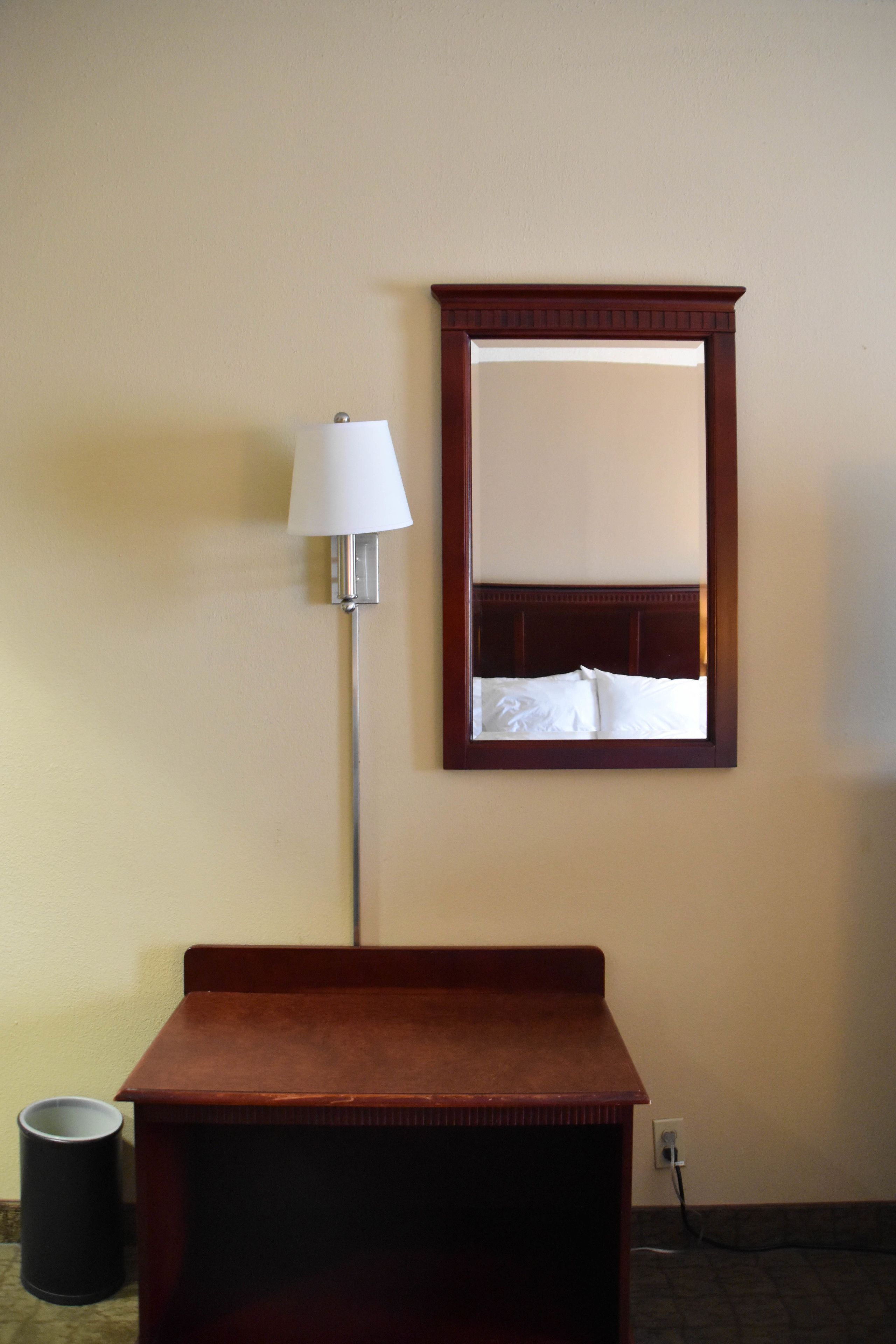 Een hotelkamer met een houten nachtkastje, een lamp, een spiegel en een prullenbak.