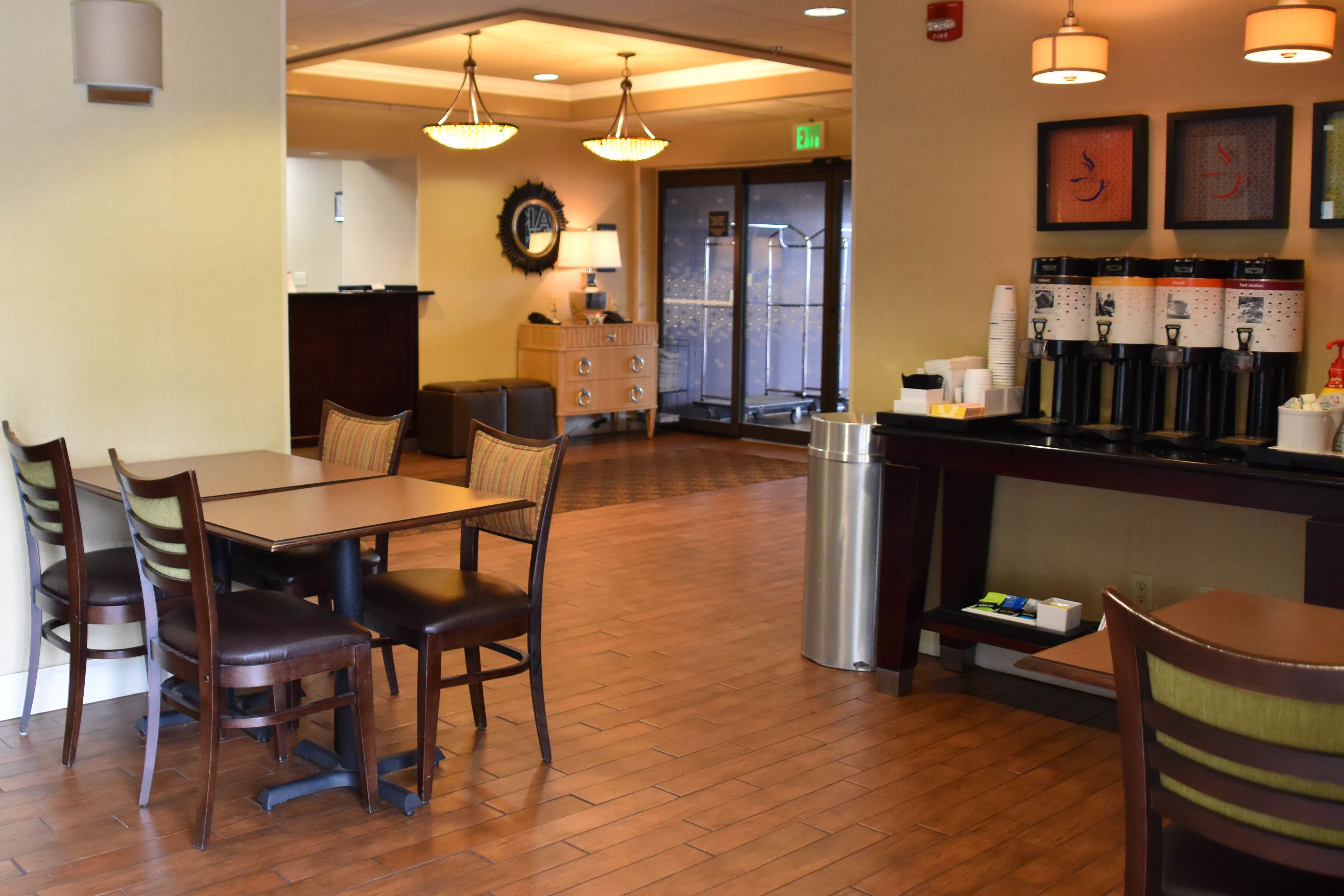 A hotel lobby with a reception desk, a coffee station, and a seating area with a table and chairs.