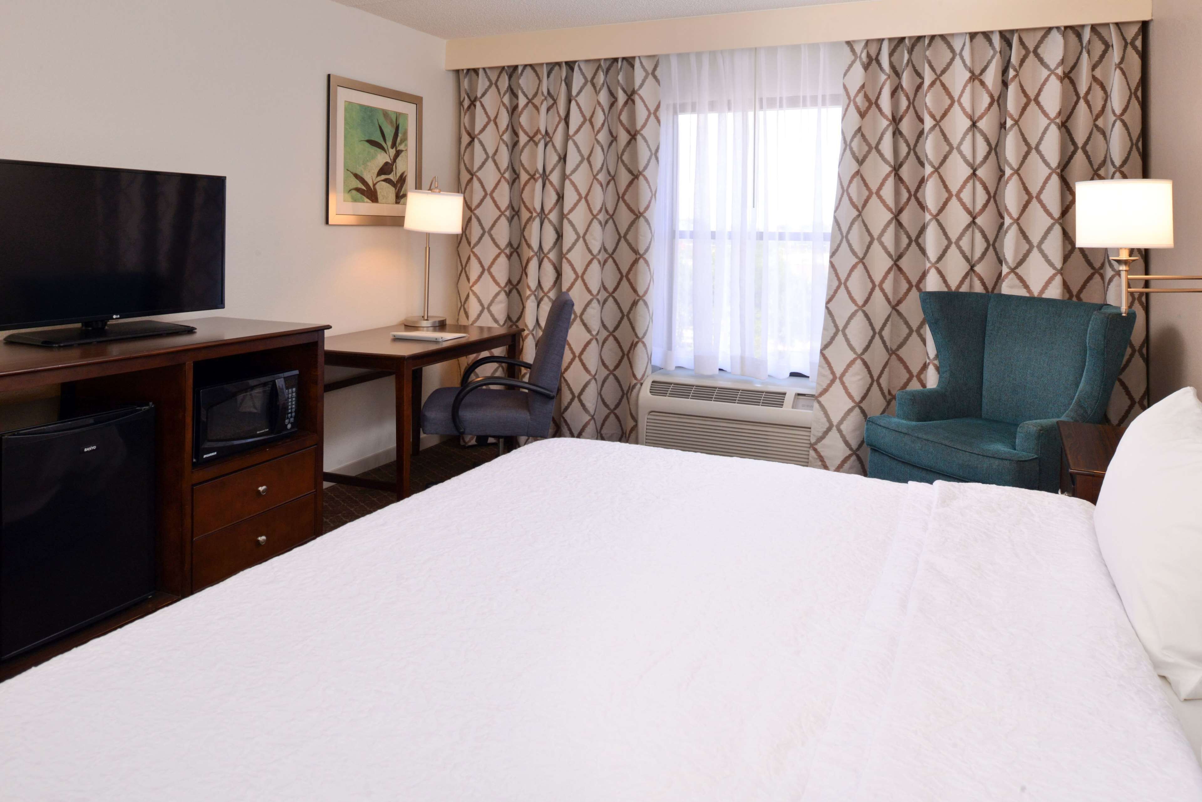 Ein Hotelzimmer mit einem Bett, einem Schreibtisch mit Fernseher, einem Sessel, einer Mikrowelle und einem Kühlschrank.