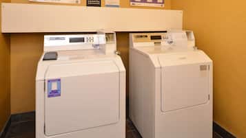 Two white front-loading washing machines in a hotel room with a tiled floor and a wooden wall.