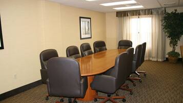 A conference room with a large table surrounded by chairs, a framed picture on the wall, and a potted plant near the window.