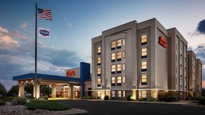 Un hôtel au design moderne, avec un drapeau américain bien visible et une enseigne indiquant « Hampton Inn & Suites ».