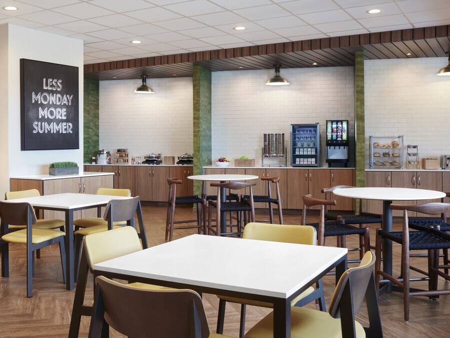 A modern dining area with multiple tables and chairs, a coffee machine, and a menu display.