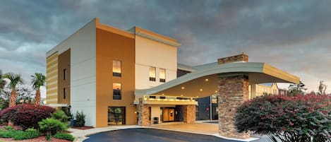 A modern hotel with a curved entrance, a stone facade, and a landscaped driveway.