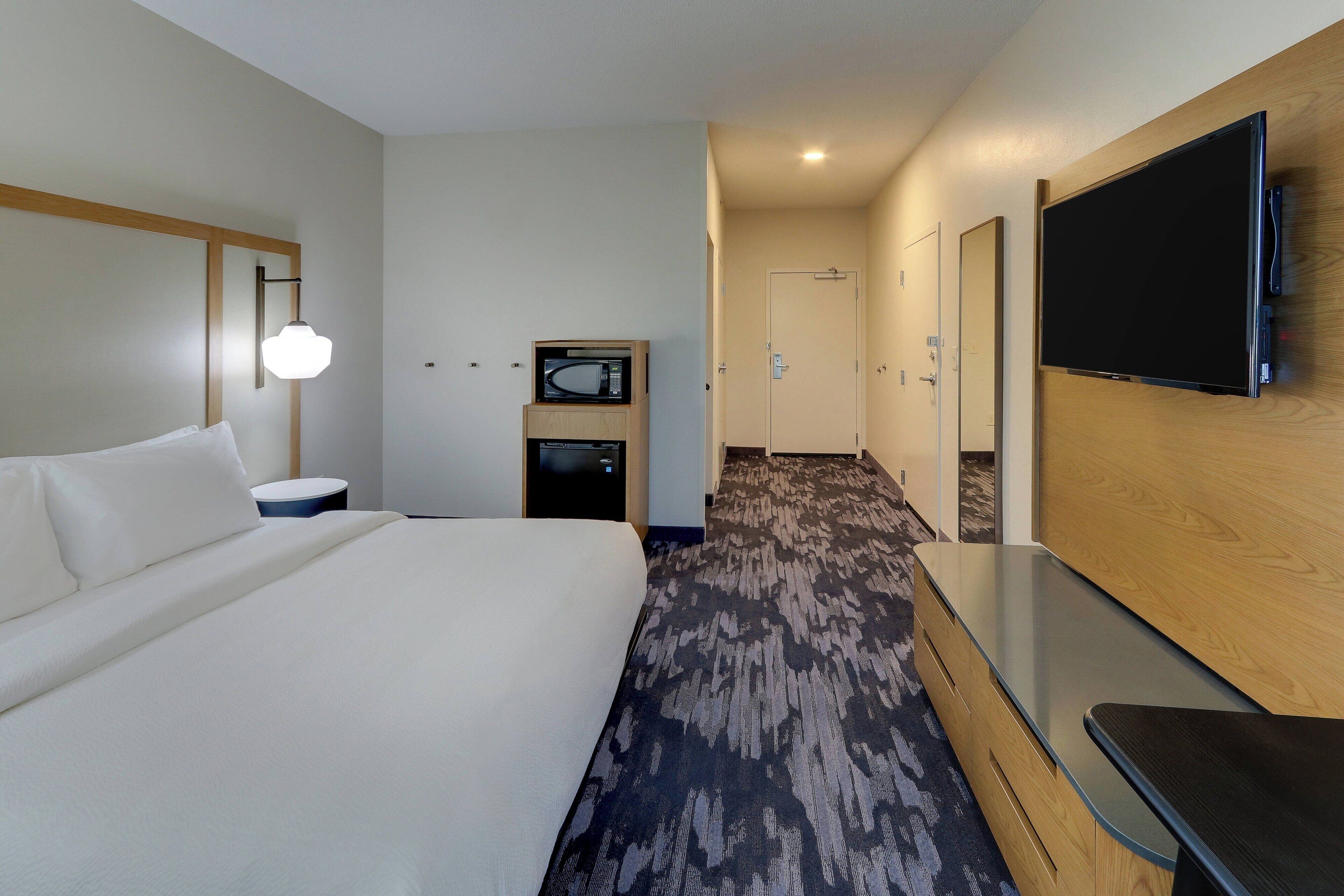 Een hotelkamer met een groot bed, een flatscreen televisie aan de muur, een magnetron en een klein tafeltje.