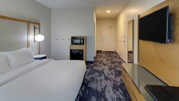 A hotel room with a large bed, a flat-screen TV mounted on the wall, a microwave, and a small table.