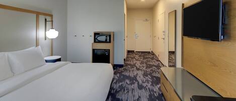 A hotel room with a large bed, a flat-screen TV mounted on the wall, a microwave, and a small table.