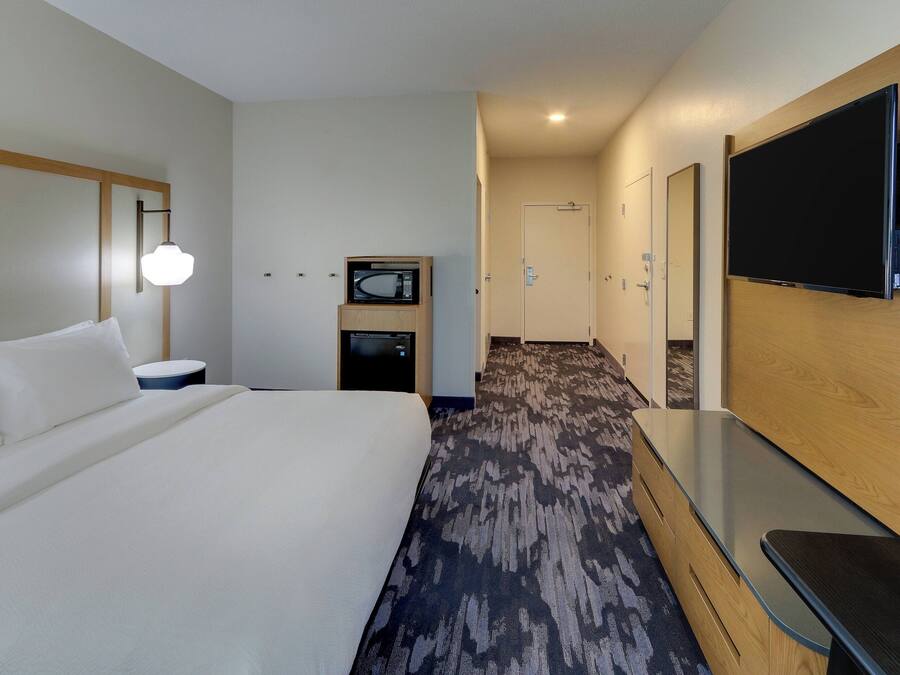 A hotel room with a large bed, a flat-screen TV mounted on the wall, a microwave, and a small table.