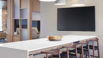 Une cuisine moderne dotée d’un grand îlot central, de luminaires suspendus et d’un téléviseur à écran plat fixé au mur.