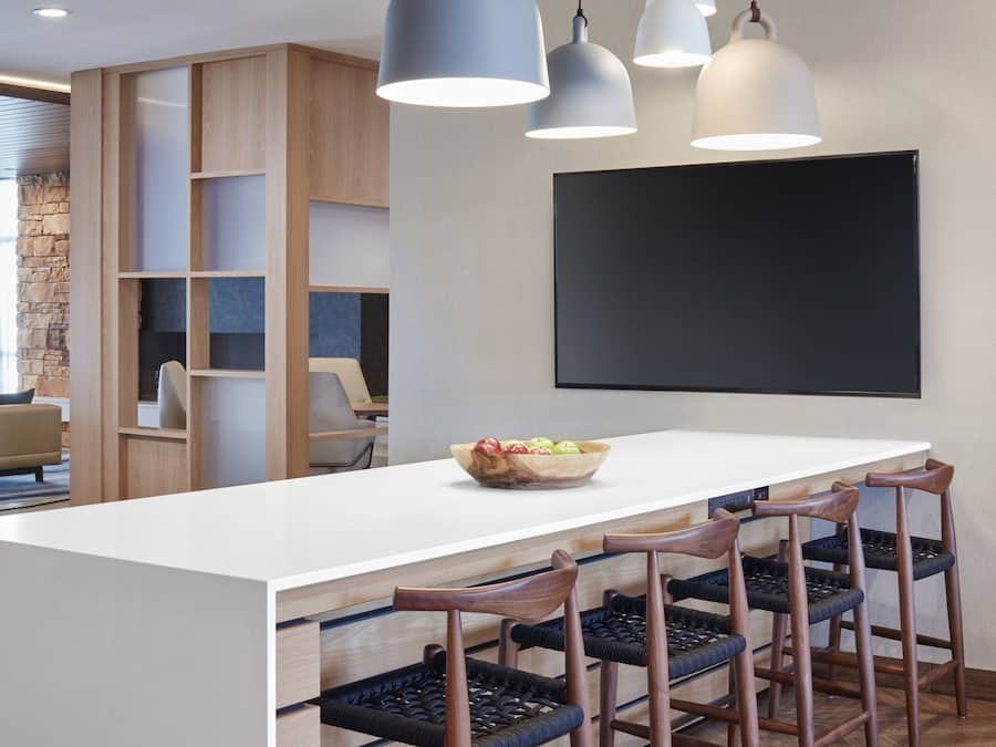 A modern kitchen with a large island, pendant lighting, and a flat-screen TV mounted on the wall.